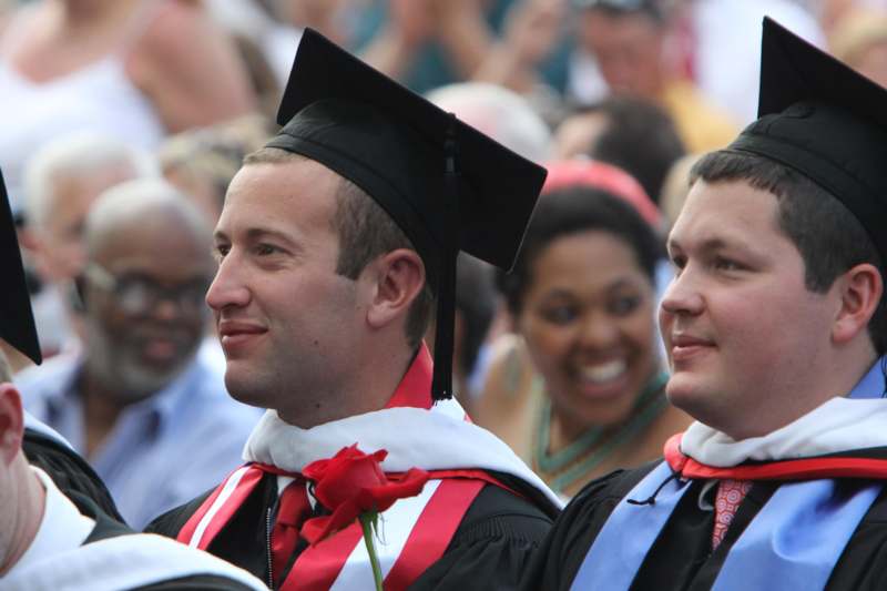 a man in graduation gown and cap with a rose in his hand