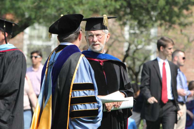 a man in a graduation gown talking to another man
