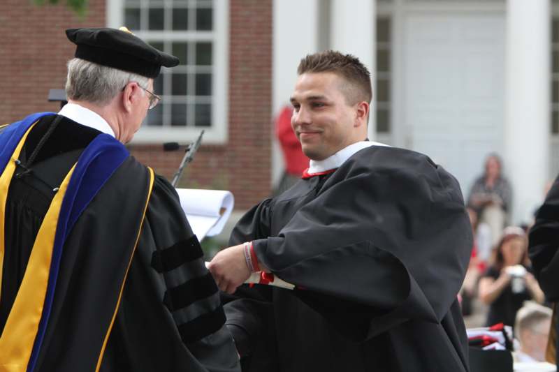 a man in a graduation gown shaking hands with a man in a cap