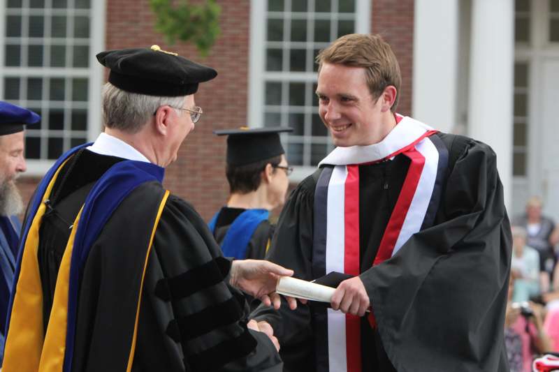 a man shaking hands with a man in graduation gown