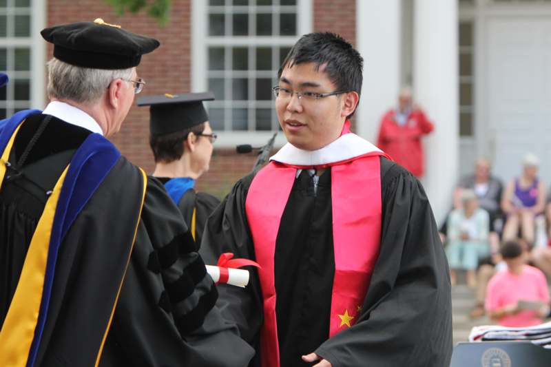 a man in a black robe and red sash standing next to a man in a black cap and gown