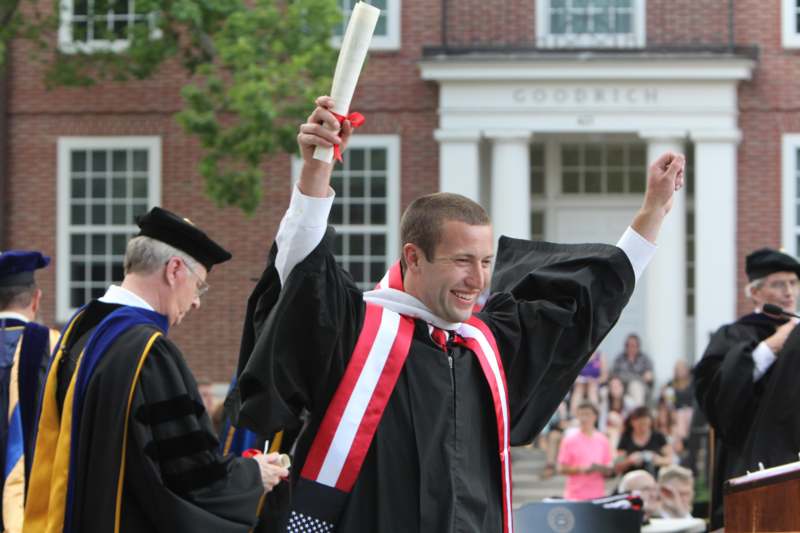 a man in a graduation gown holding up a diploma