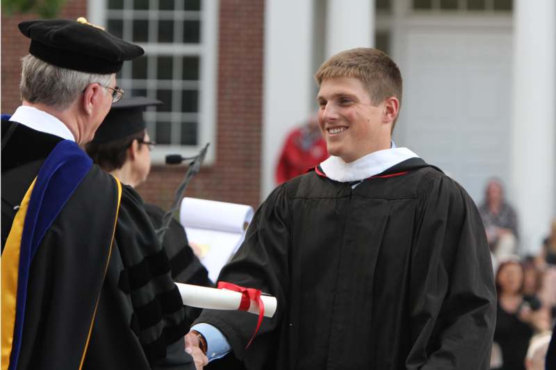 a man in a graduation gown shaking hands with another man