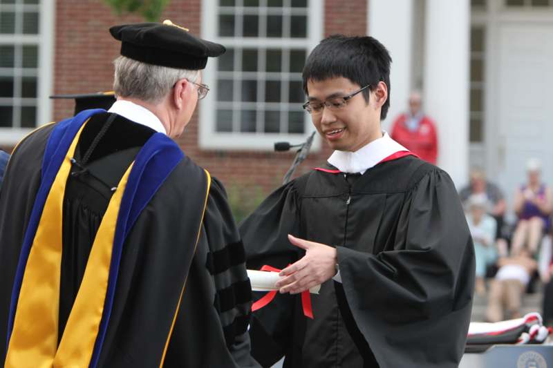 a man in a graduation gown talking to a man in a black cap