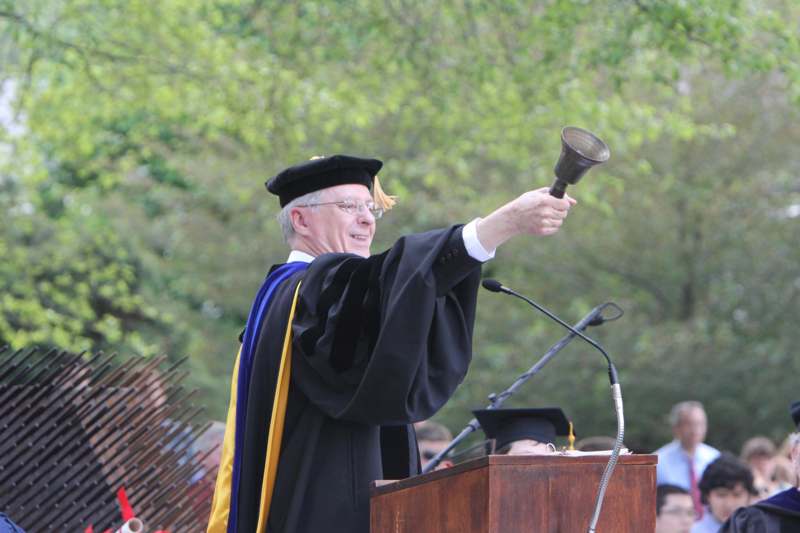 a man in a graduation gown holding a bell