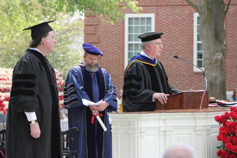 a group of men in graduation gowns and caps standing at a podium