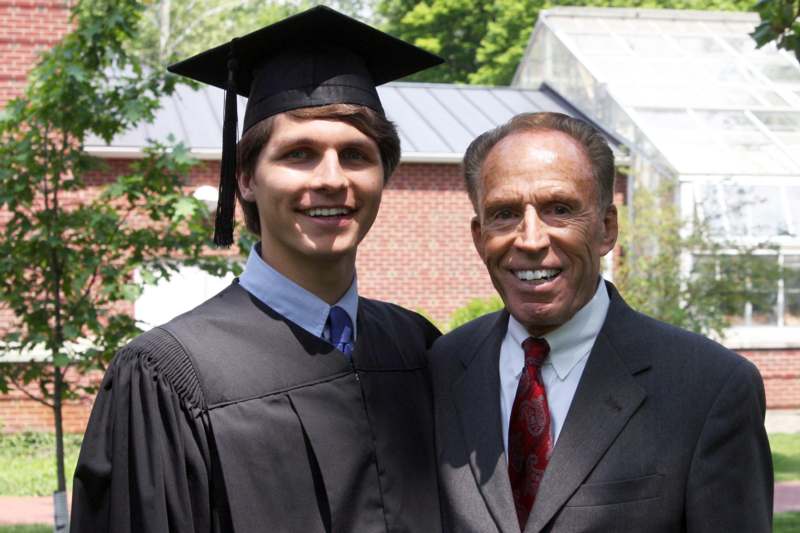 a man in a graduation gown and cap standing next to a man in a suit