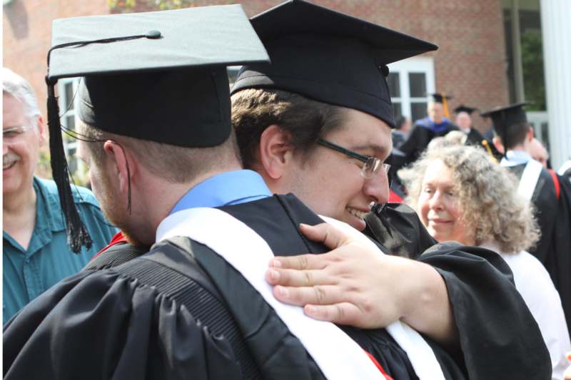 a man in graduation gown hugging another man
