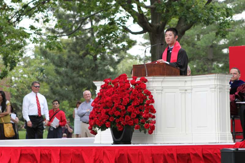 a man in a graduation gown standing at a podium with a microphone