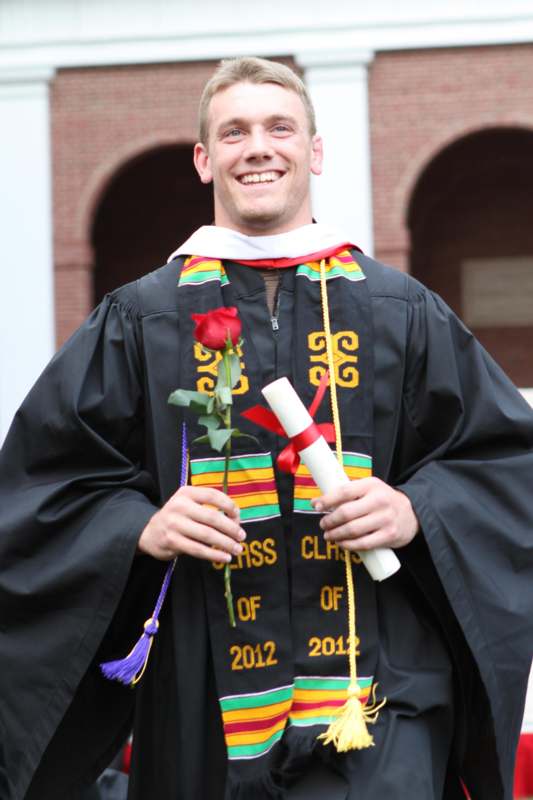 a man wearing a graduation gown holding a rose and diploma