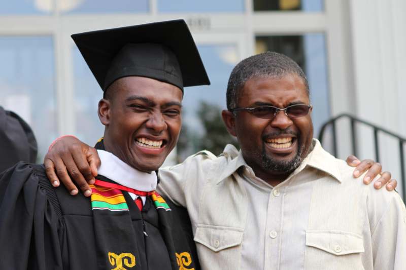 a man in a graduation gown and cap smiling with another man in a building