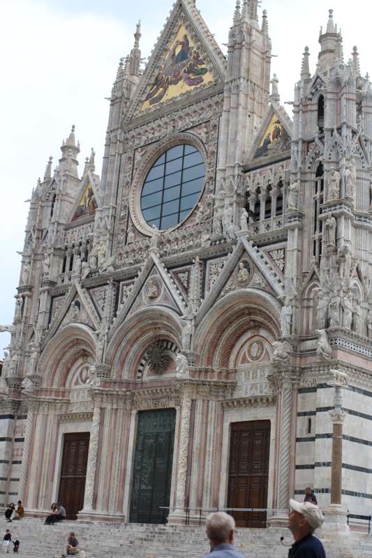 a large ornate building with a round window with Siena Cathedral in the background