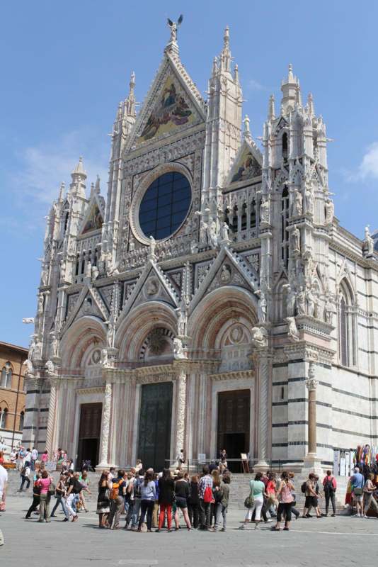 a large ornate building with people walking around with Siena Cathedral in the background