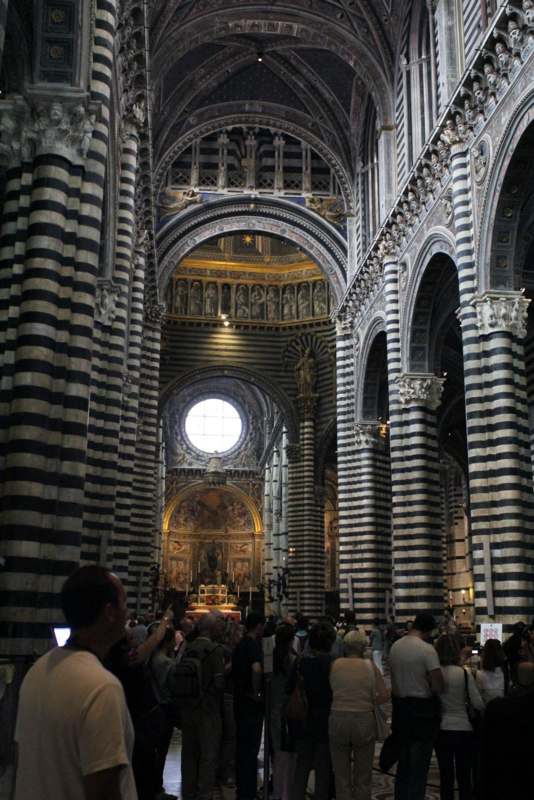 a large building with many columns and a crowd of people with Siena Cathedral in the background