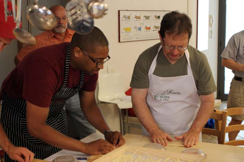 a group of men in aprons cutting pasta