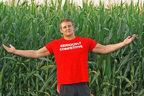 a man in a red shirt with his arms out in front of a corn field