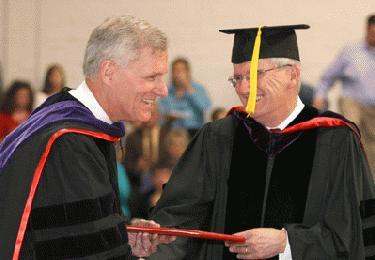 a man in graduation gowns shaking hands with another man
