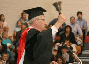 a man in a graduation cap and gown raising a bell