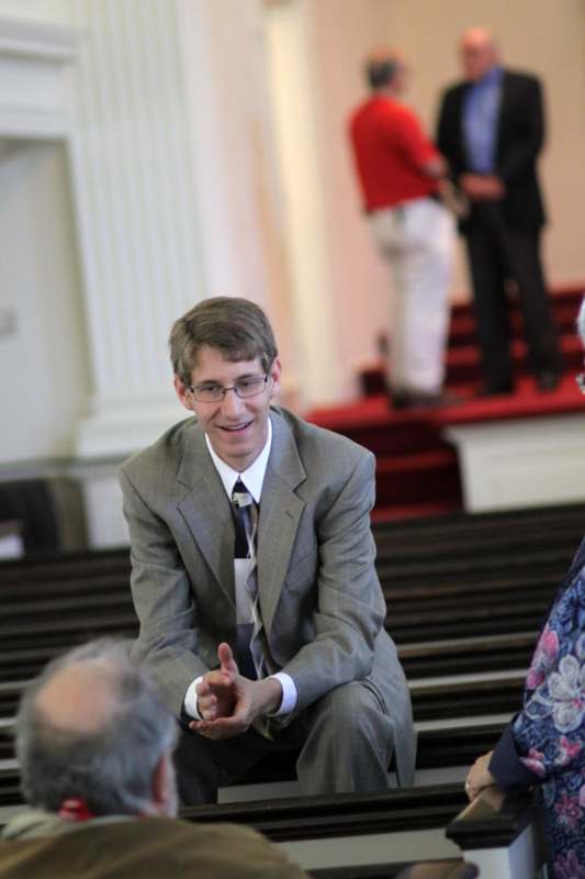 a man in a suit and tie sitting on pews