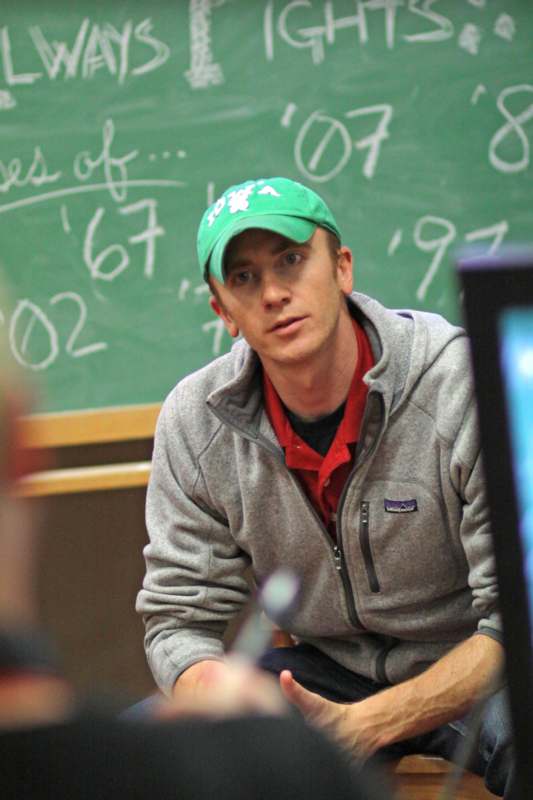 a man in a green hat sitting in front of a chalkboard