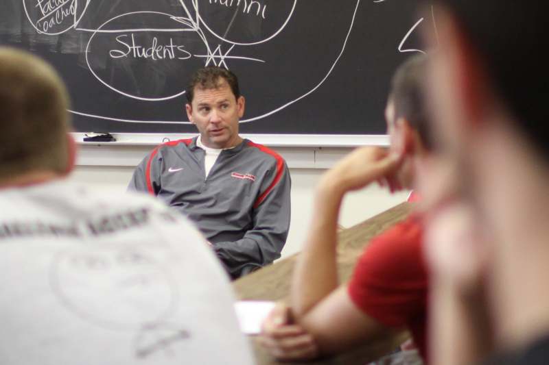 a man in a grey shirt sitting in front of a blackboard