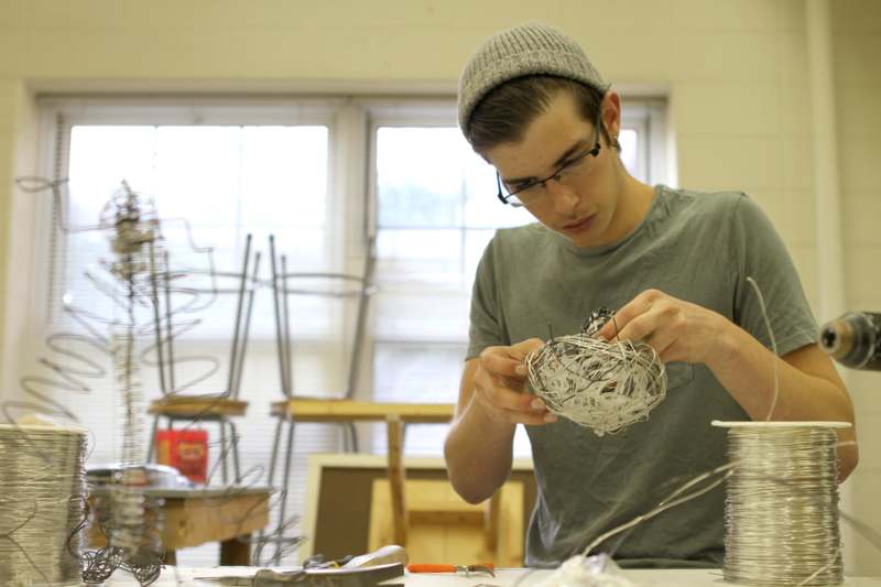 a man in a hat and glasses working on a wire sculpture