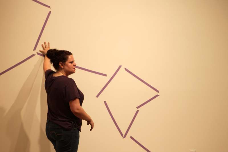 a woman standing next to a wall with purple lines