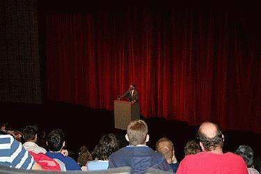 a man standing at a podium with a crowd watching