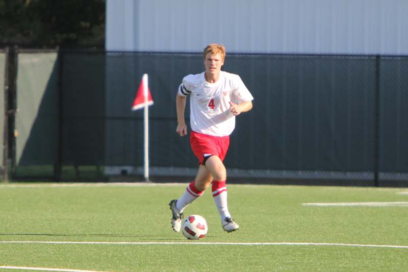 a man in a white shirt and red shorts running with a football ball