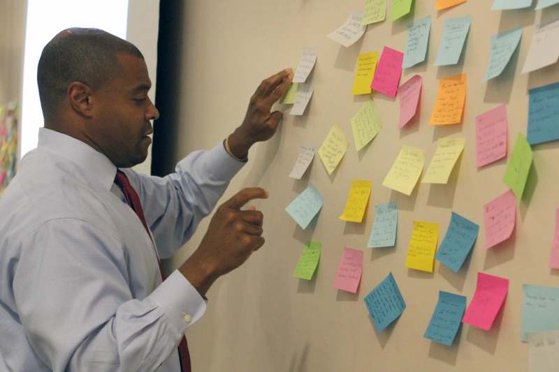 a man pointing at a wall with many sticky notes