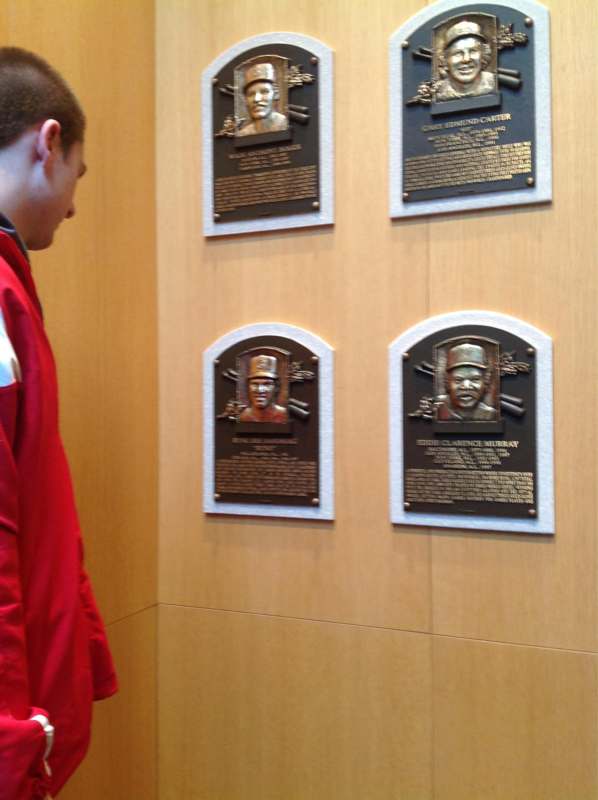 a man looking at plaque on a wall with National Baseball Hall of Fame and Museum in the background