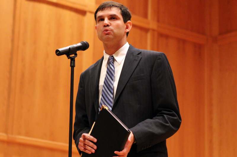 a man in a suit holding a book and standing in front of a microphone