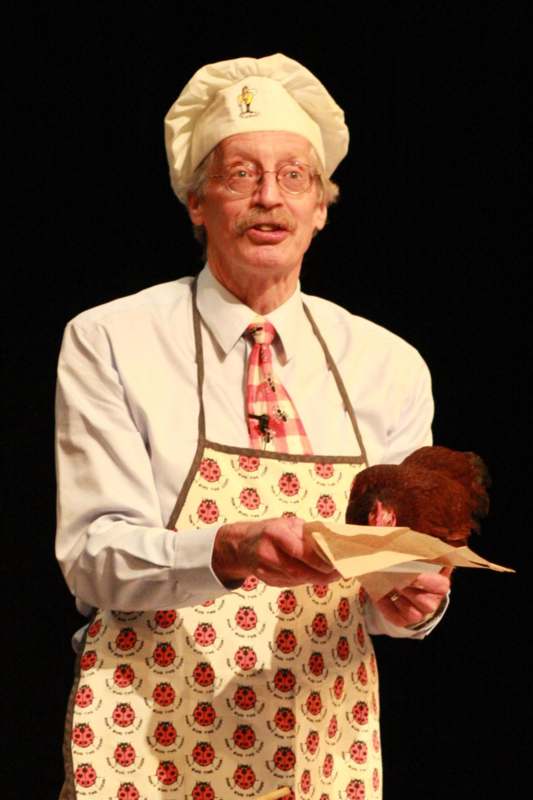 a man wearing a chef hat and apron holding a chicken