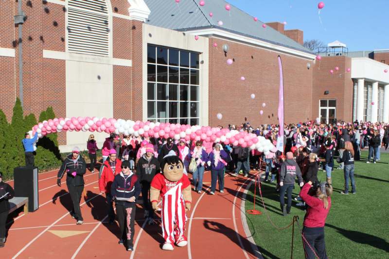 a group of people walking on a track with pink and white balloons