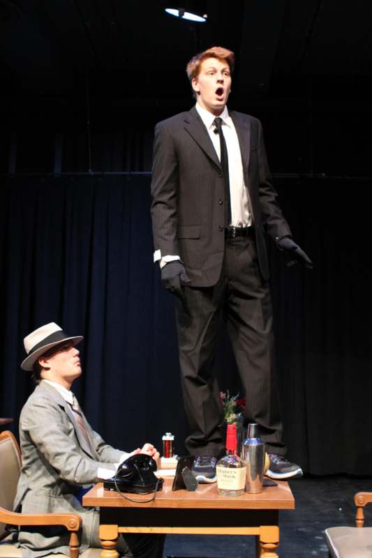 a man in a suit standing on a table with another man in a hat