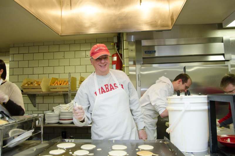 a man in a red hat and white apron making pancakes