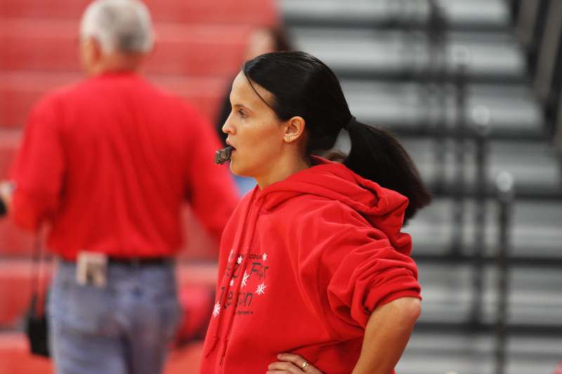 a woman in a red sweatshirt with a whistle in her mouth