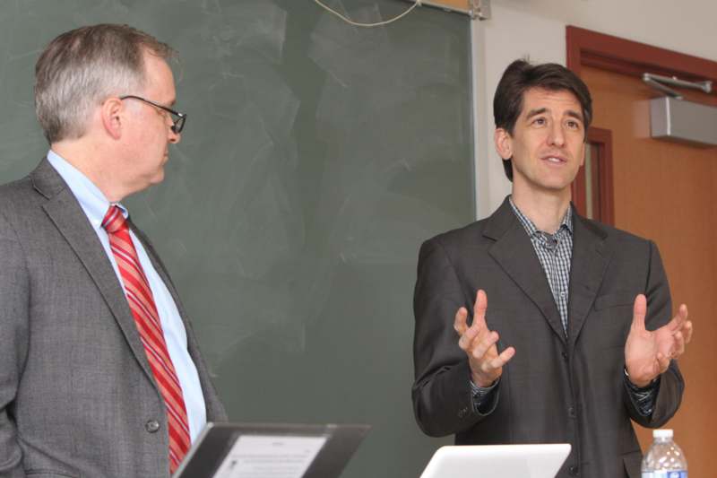 a man in suit standing next to another man in front of a chalkboard