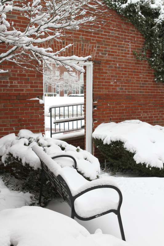 a snow covered bench in front of a brick building