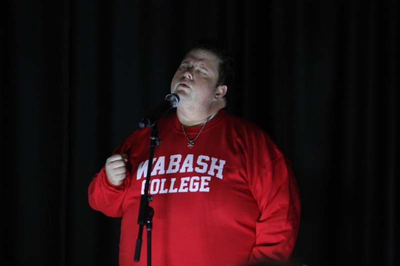 a man in a red shirt singing into a microphone