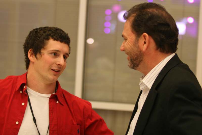 a man in a red shirt and black suit talking to another man