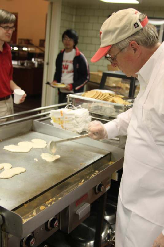 a man in a white coat and hat cooking pancakes