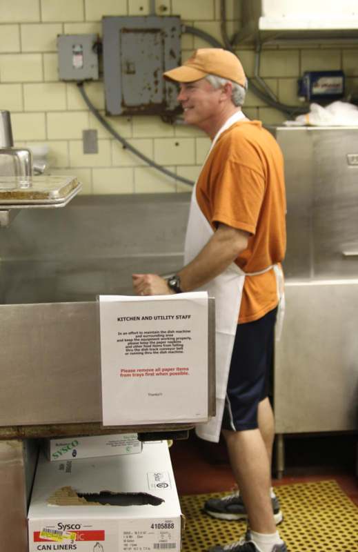 a man in an orange shirt and apron standing in a kitchen