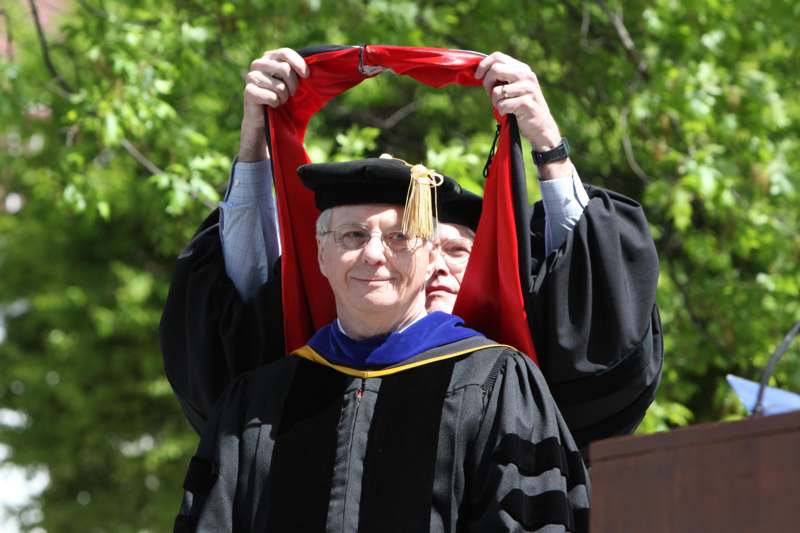a man in a graduation gown holding up a red scarf