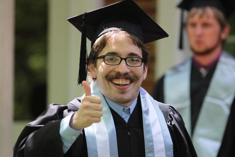 a man in a graduation gown giving a thumbs up