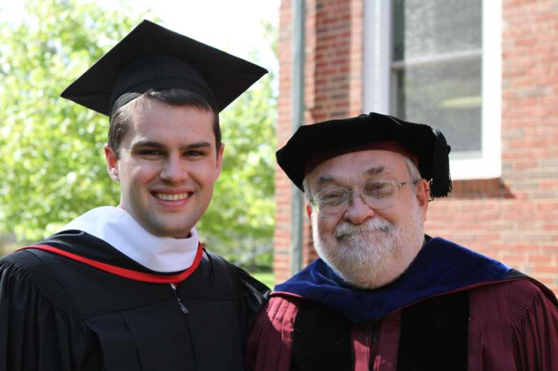 a man in graduation gown and cap standing next to another man in a cap and gown