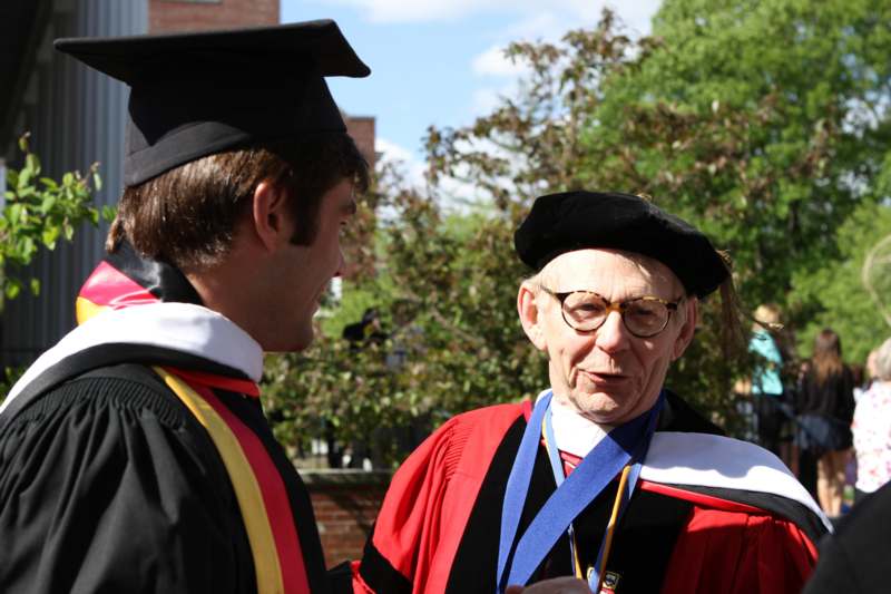 a man in graduation gown talking to another man