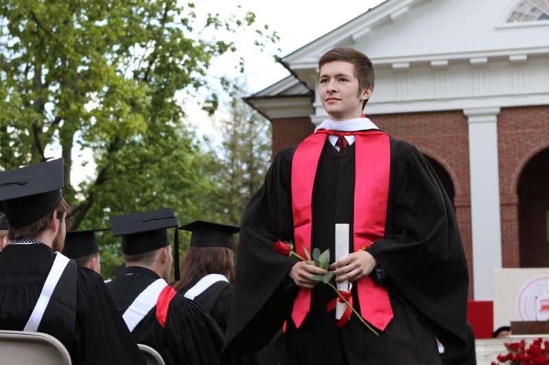 a man in a black gown holding a rose and a diploma