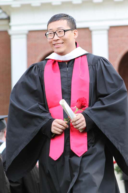 a man wearing a graduation gown and holding a rose