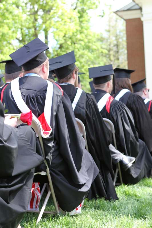 a group of people in graduation gowns and caps sitting in chairs